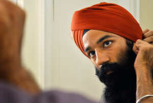 Sikh man looking in mirror and tying his red turban